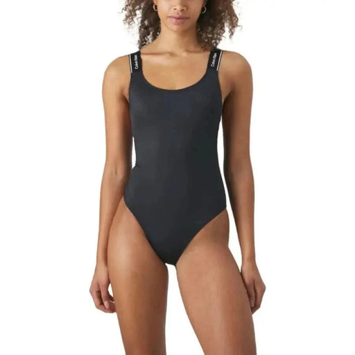 Black one-piece swimsuit with thin straps worn by a woman with curly hair from Calvin Klein