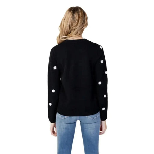 Blonde woman in blue jeans wearing Vero Moda black sweater with white polka dot sleeves