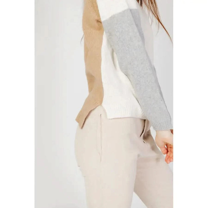 Color-blocked sweater with beige, white, and gray sections worn with light-colored pants