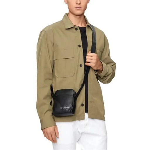 Khaki button-up shirt jacket with large pockets over a black top, displayed with Calvin Klein Men Bag