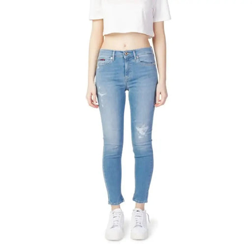 Model wearing light blue distressed Tommy Hilfiger skinny jeans with white cropped top and sneakers