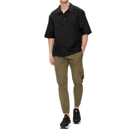 Man in Calvin Klein black short-sleeved shirt, olive cargo pants, and black sneakers