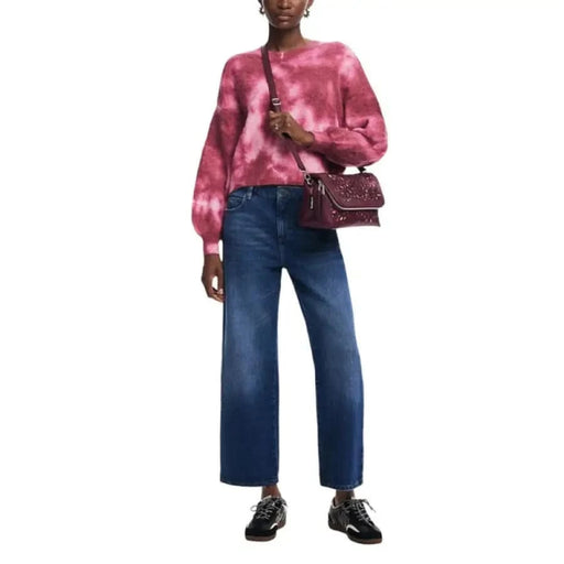 Person in pink tie-dye sweater and blue jeans with Desigual burgundy handbag