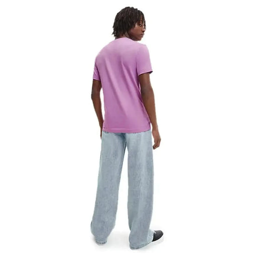 Person in Calvin Klein purple t-shirt and light blue jeans standing with back to camera