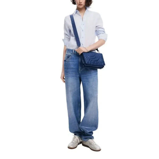 Person in white sweater and wide-leg jeans with Desigual blue shoulder bag