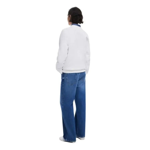 Person wearing white Desigual sweatshirt and blue jeans, standing with back turned