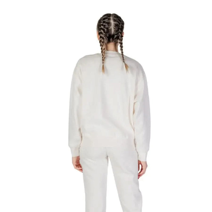 Person in white sweatsuit with braided hair from behind in Guess Active women’s collection