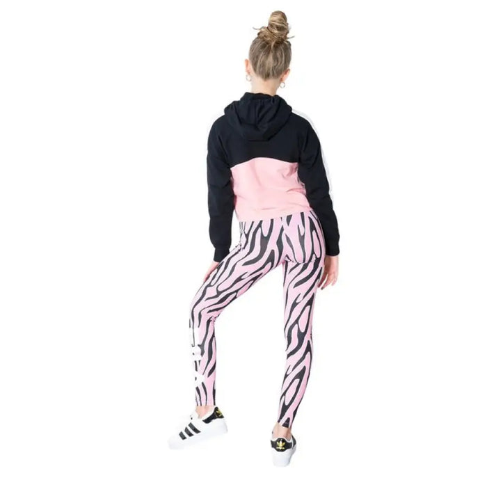 Person in zebra-print leggings and pink top with black hooded jacket by Fila