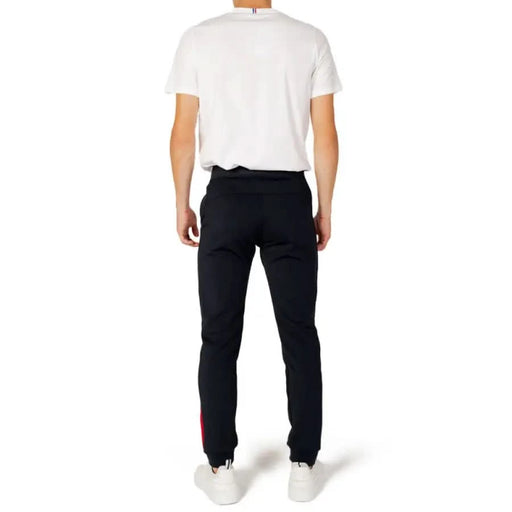 Rear view of a person in white shirt, black trousers with red stripes - Le Coq Sportif Men Trousers