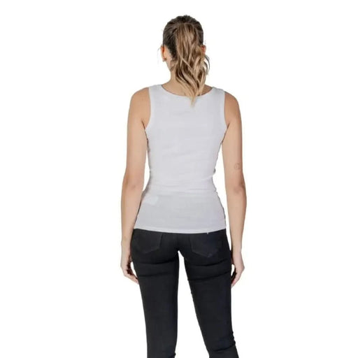 Back view of a woman in a white sleeveless top and black pants for Guess product