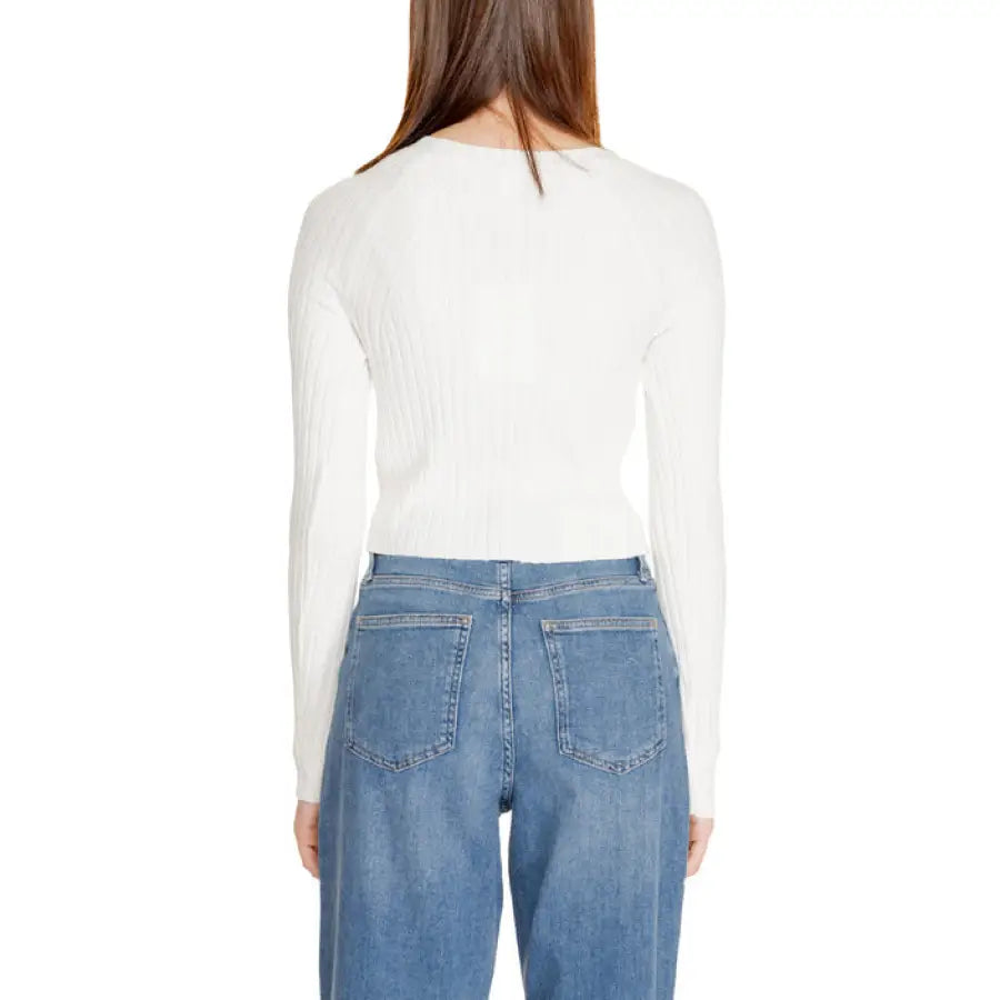 Back view of woman in white long-sleeved top and blue jeans by Only Women Knitwear