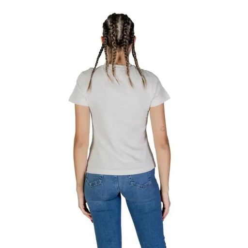 Back view of woman in Guess Active white t-shirt and blue jeans with braided hair