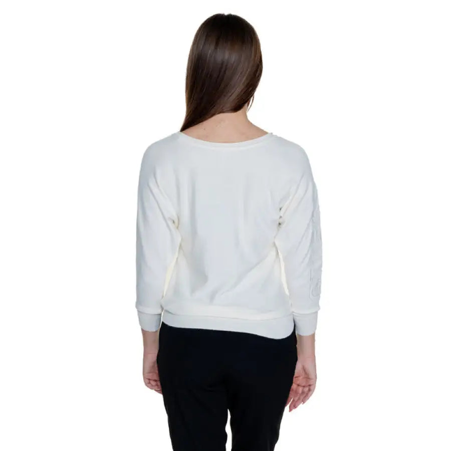 White long-sleeved sweater by Guess, worn by person with long dark hair, viewed from behind