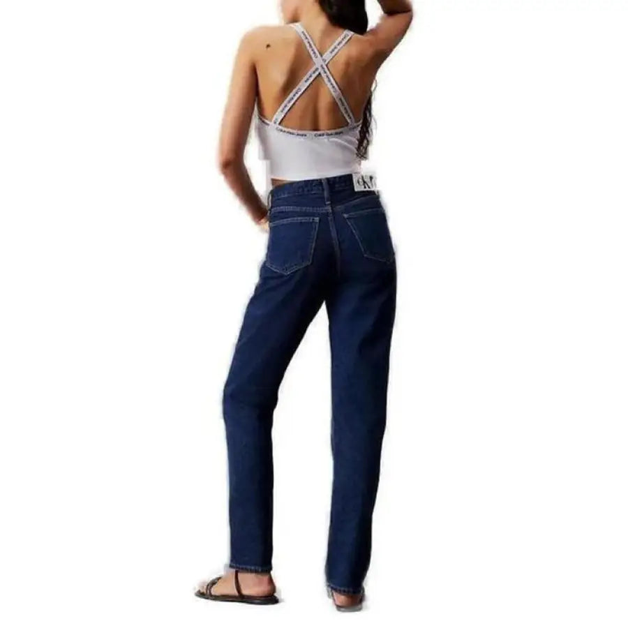 Woman in high-waisted blue jeans, white crop top with crisscross straps - Calvin Klein Jeans