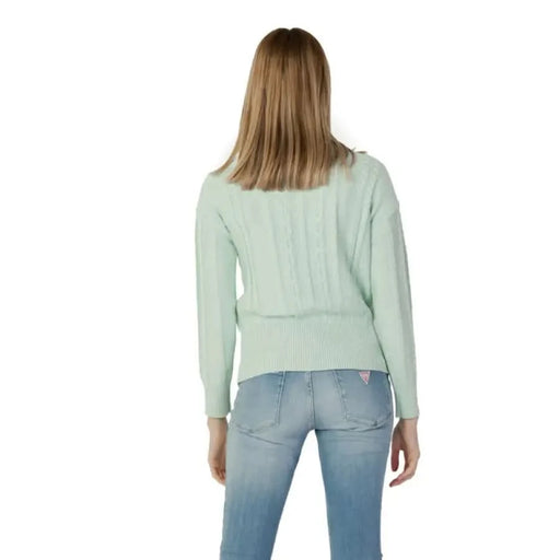 Woman in mint green sweater and light blue jeans from behind, showcasing Guess Knitwear