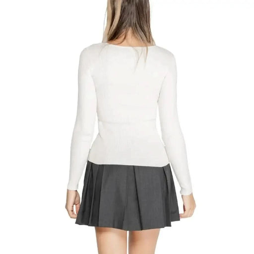 Woman in white long-sleeved top and dark pleated skirt showcasing Morgan De Toi knitwear